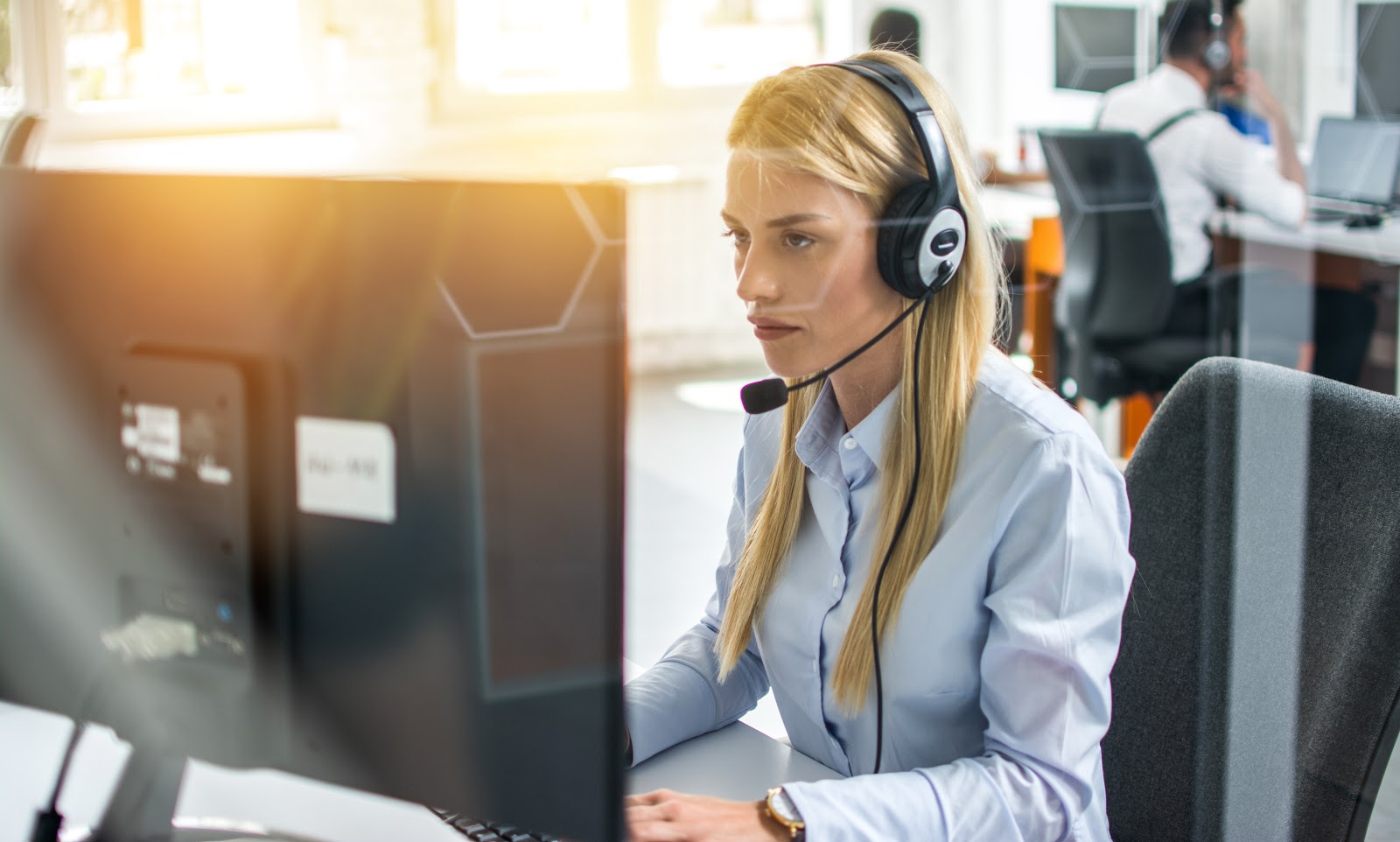 a young woman speaking through a headset while working on an office computer