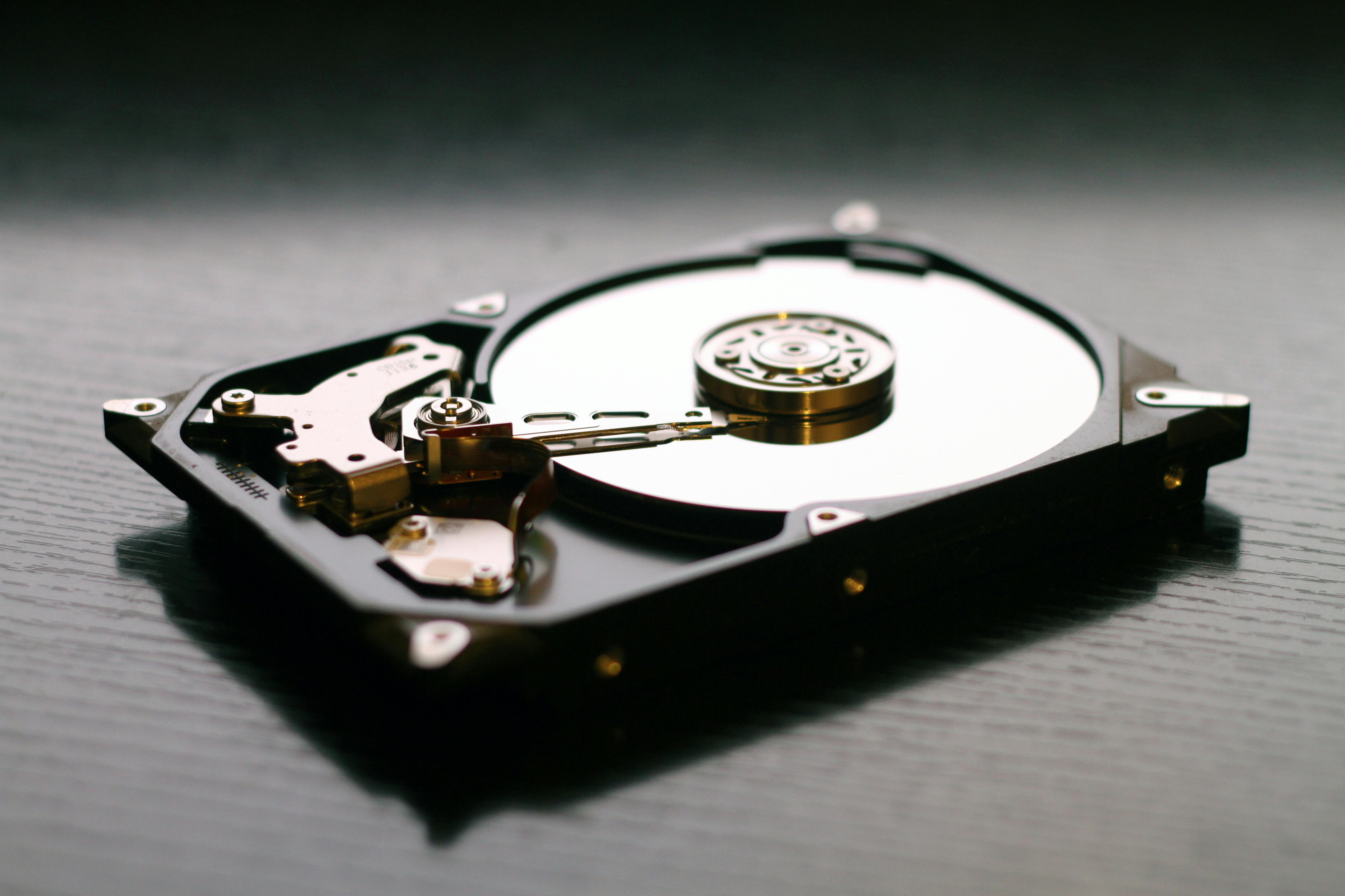 A hard disk in the shape of a rectangular box with its internal components exposed. It consists of a circular shiny plate with a read/write head.